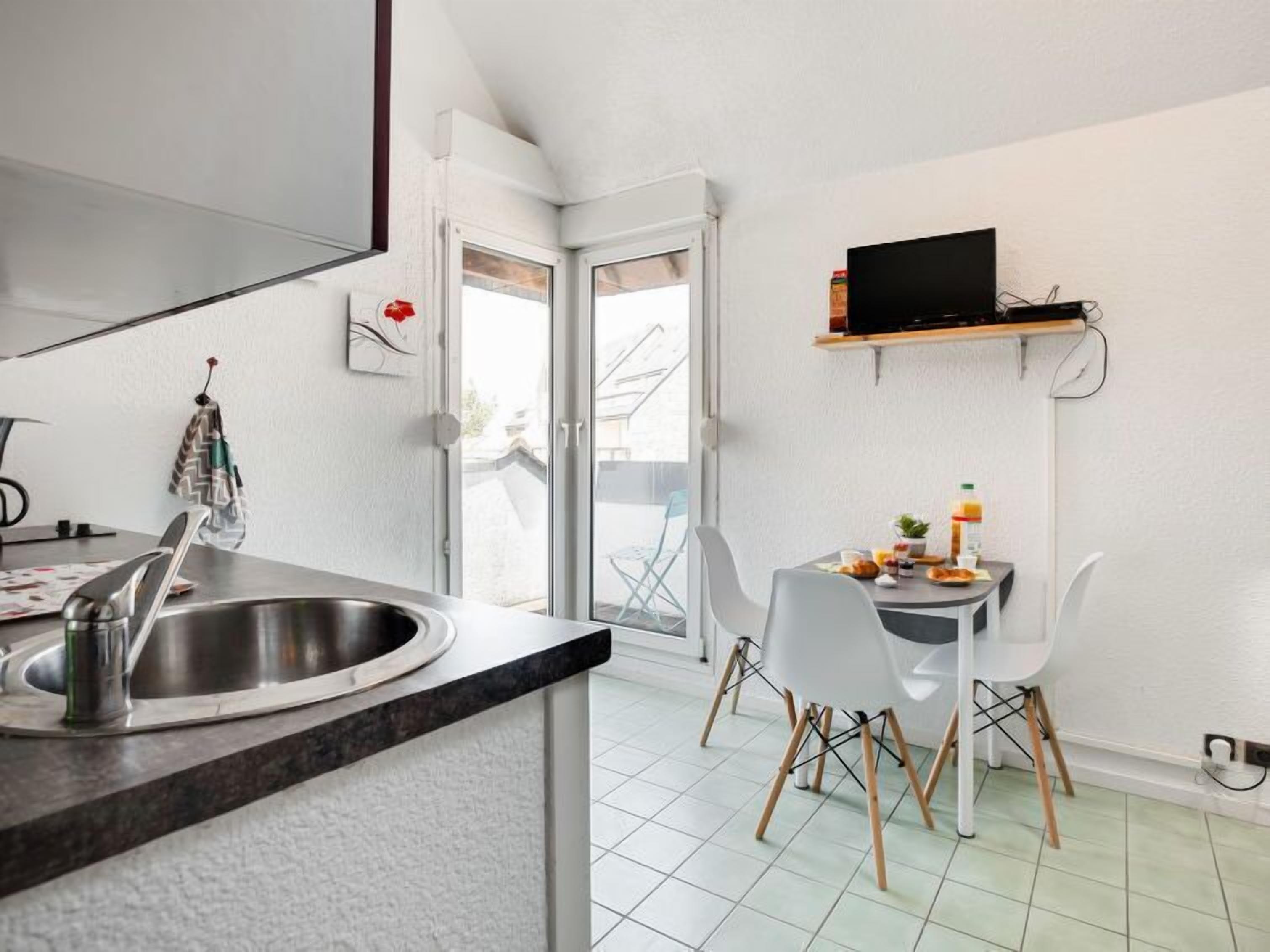 Eine moderne Küche mit Spüle, einem Esstisch mit Stühlen und einem über dem Tisch montierten Fernseher.