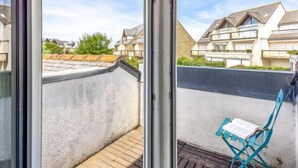 A balcony with a view of neighboring houses, a wooden floor, and a blue chair with a book. - Maison Port En Dro by Interhome (Carnac)