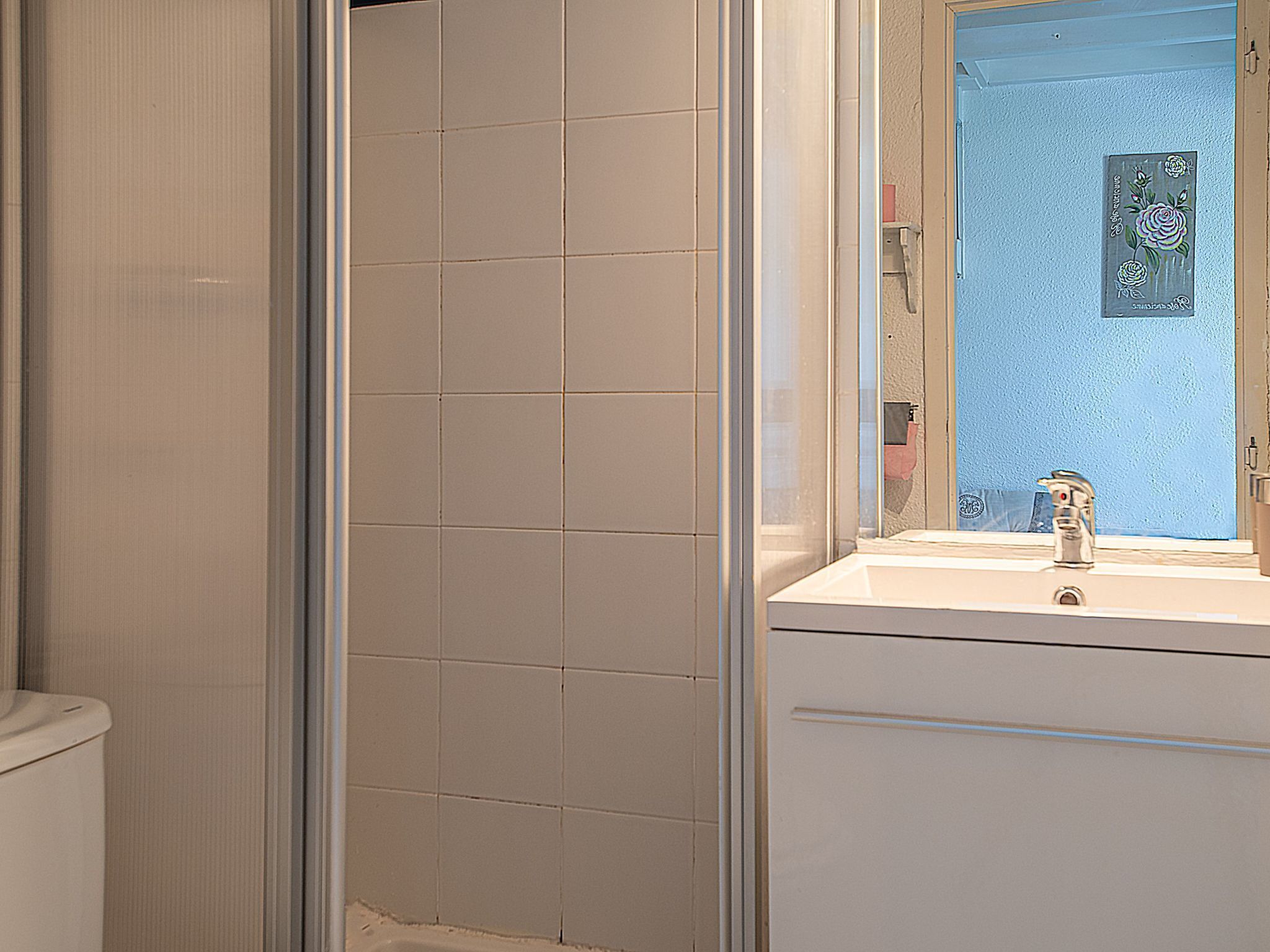 Een badkamer met een witte betegelde douche, een wastafel met spiegel en een blauwe muur.