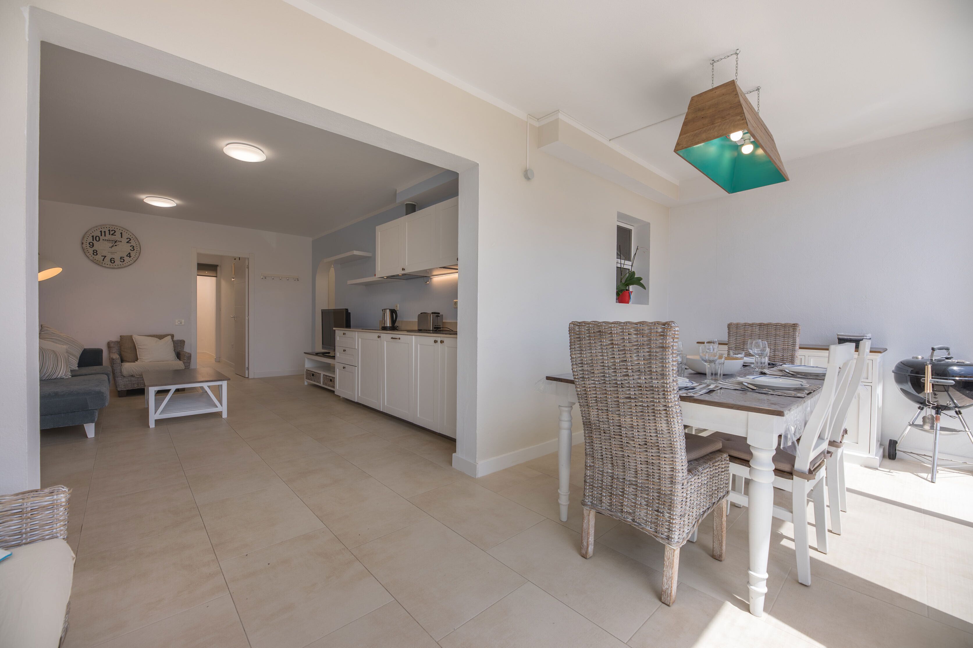 A spacious living area with a dining table, wicker chairs, a sofa, and a kitchen in the background.