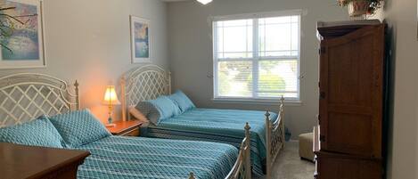 A bedroom with two beds, a ceiling fan, a window with blinds, and a wooden cabinet.