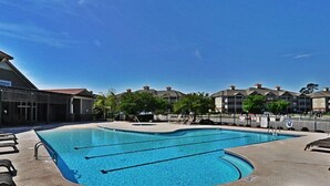 A swimming pool with multiple lanes, surrounded by lounge chairs and a building with a red roof. - 1202 Crow Creek Drive (Calabash)