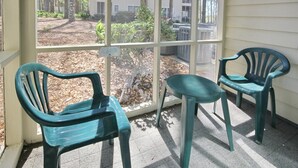 Een overdekte buitenruimte met twee groene plastic stoelen en een raam met uitzicht op een tuin en een gebouw.