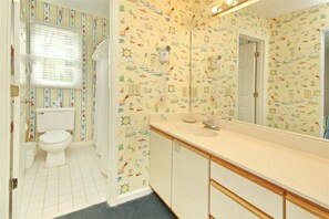 A bathroom with a toilet, sink, and mirror. The walls have a colorful pattern. - 201 River Creek Sea Trail (Sunset Beach)