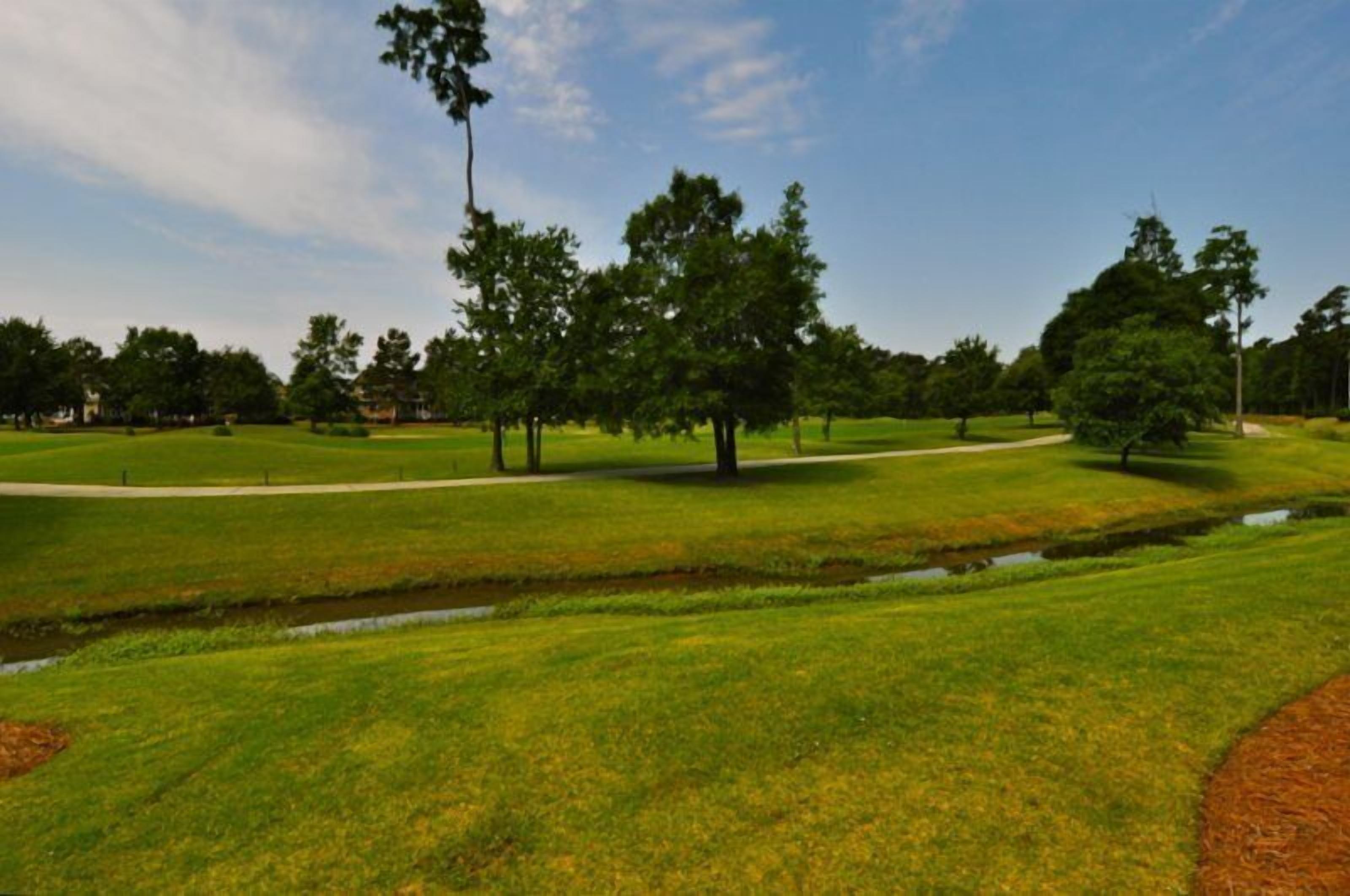 Un parcours de golf avec une pelouse bien entretenue, des arbres et un ciel dégagé.