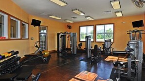 Une salle de sport équipée de divers appareils d’exercice, dotée de grandes fenêtres et d’un plafond orné de multiples luminaires.