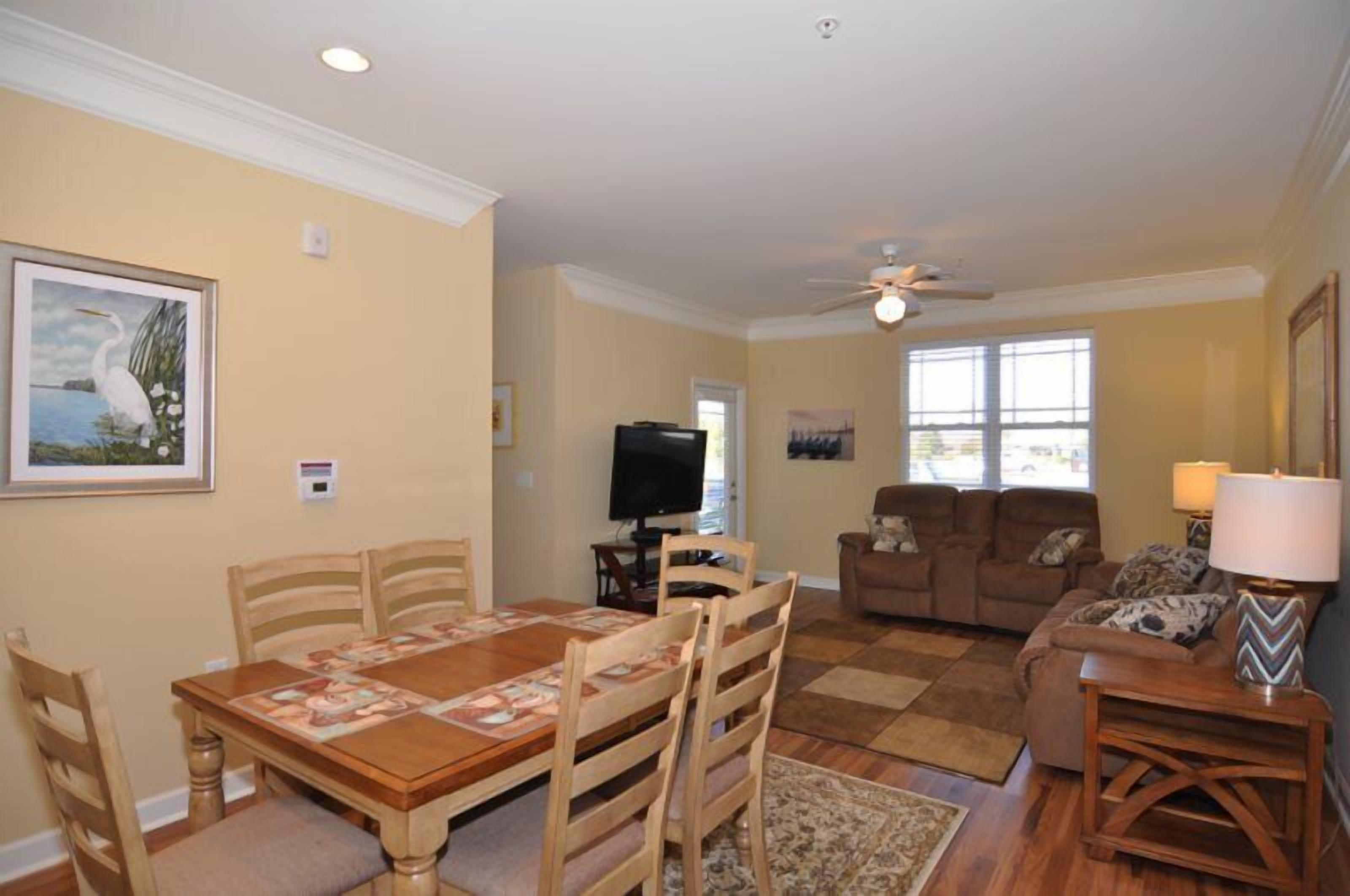A living room with a wooden dining table, chairs, a sofa, and a television.