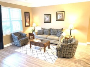 A living room with a sofa, two armchairs, a coffee table, and two lamps. - 24006 Woodlands Way (Calabash)