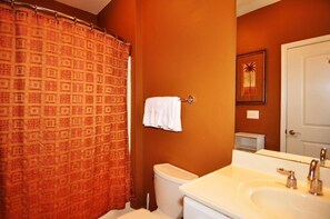 A bathroom with a patterned shower curtain, a toilet, a sink with two faucets, and a mirror. - 24006 Woodlands Way (Calabash)