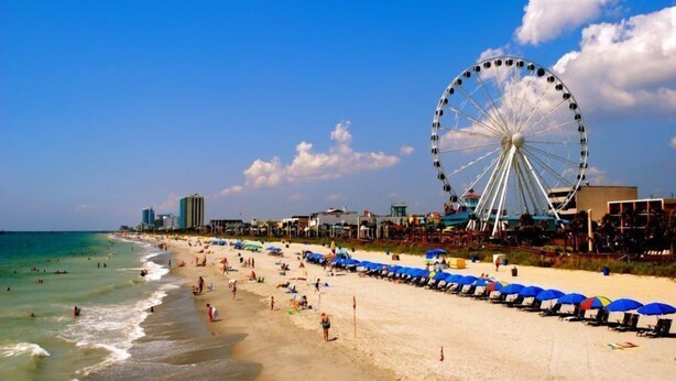 Une plage avec une grande roue, des parasols et une étendue de sable.