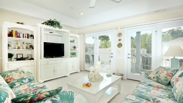 A living room with a television, floral sofas, a coffee table, and a bookshelf. - 805 Colony II (Sunset Beach)