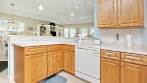 A modern kitchen with wooden cabinets, a white dishwasher, and pendant lighting. - 805 Colony II (Sunset Beach)