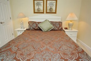 A neatly made bed with a patterned bedspread, two bedside lamps, a nightstand with a clock, and two framed pictures on the wall.