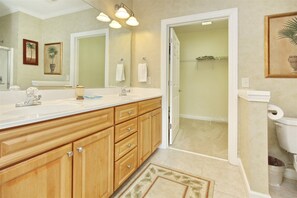 A bathroom with a large wooden vanity, a sink, a mirror, and a toilet. There are towels hanging on the wall and a shower area visible through an open door.