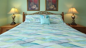 A bed with a striped bedspread, two nightstands, two wall-mounted lamps, and two framed paintings of vases and a palm tree. - 805 Colony II (Sunset Beach)