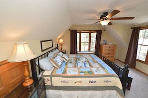 Cozy retreat with a large bed, nightstand, dresser, and ceiling fan, featuring a nautical-themed quilt.