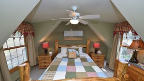 A bedroom with a wooden bed frame, a quilt, two bedside tables with lamps, a ceiling fan, and a window with curtains.
