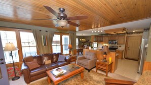 A spacious living room with a ceiling fan, a brown leather sofa, a wooden coffee table, and a patterned rug.