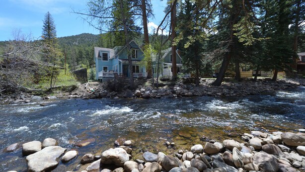 A house by a clear stream with a wooden deck and a white fence.