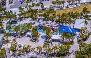 An aerial view of a resort area with a swimming pool, palm trees, and a covered seating area.