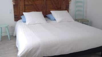 A bed with a wooden headboard, a small stool, and a chair in a room with white walls and wooden flooring.