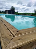 Una piscina con solárium de madera y escalera metálica.
