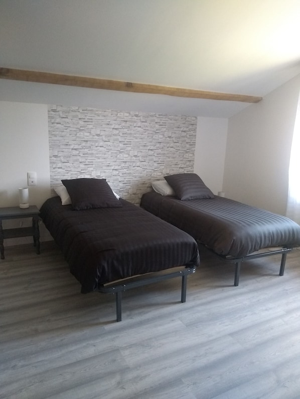 Una habitación con dos camas individuales, una mesita de noche con lámpara, un interruptor de luz en la pared y techo con vigas de madera.