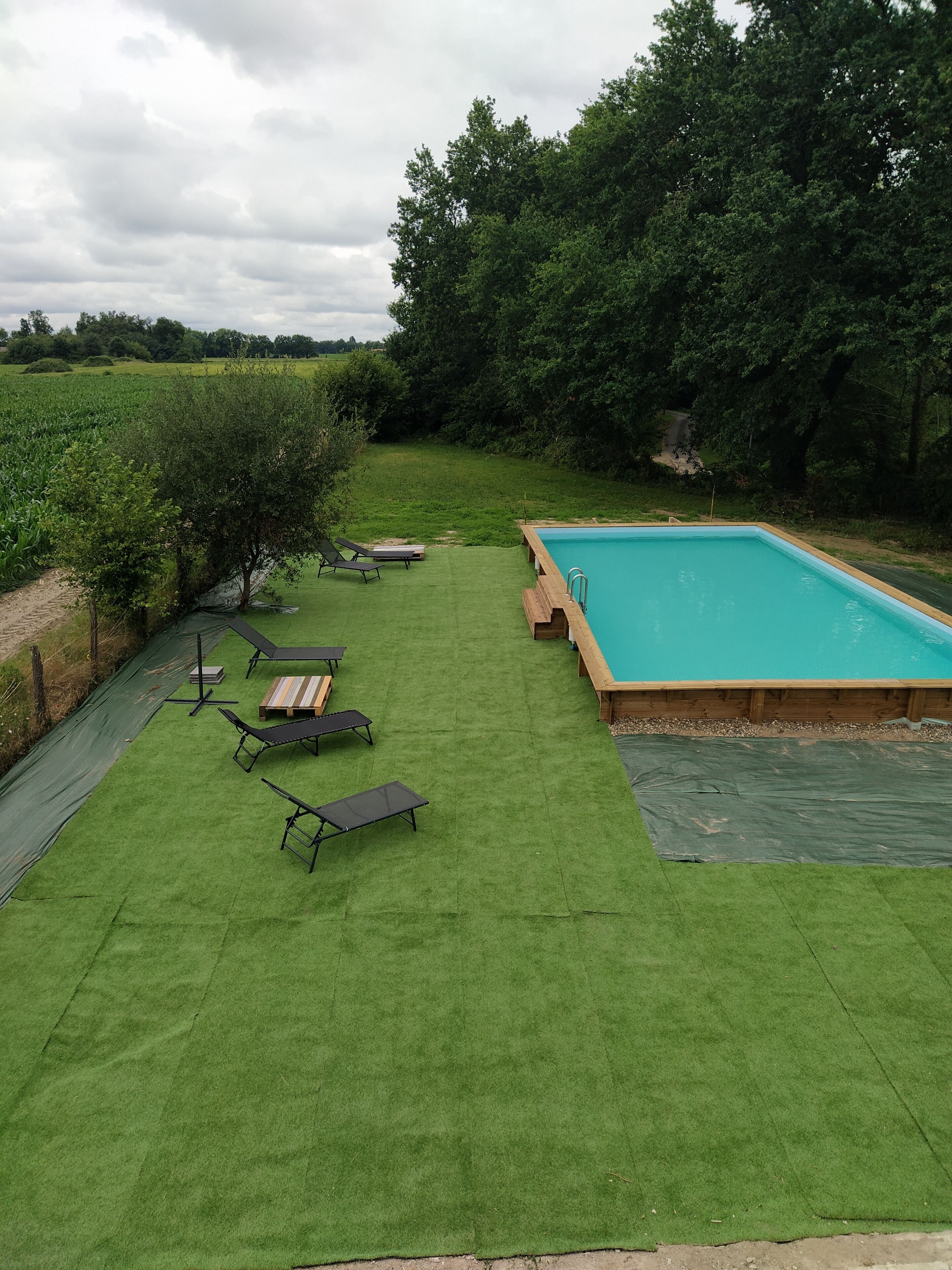 A backyard with a swimming pool, green artificial grass, and lounge chairs.