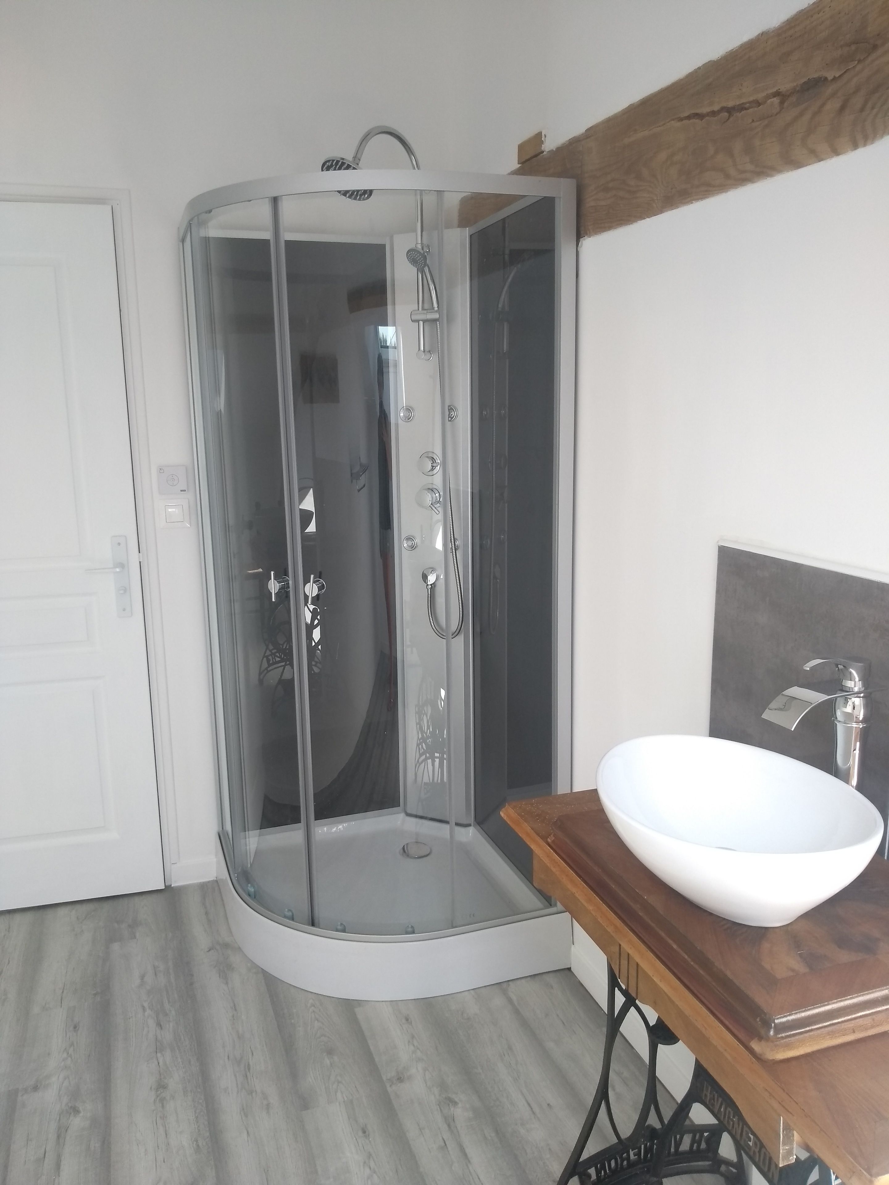 A corner bathroom with a glass-enclosed shower, a white sink, and a wooden vanity.