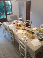 Mesa de desayuno dispuesta con diversos platos, incluyendo pan, fruta y bebidas, en una habitación con vistas a zonas verdes.