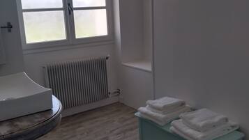 A bathroom with a window, radiator, sink, and a stack of towels on a cabinet.