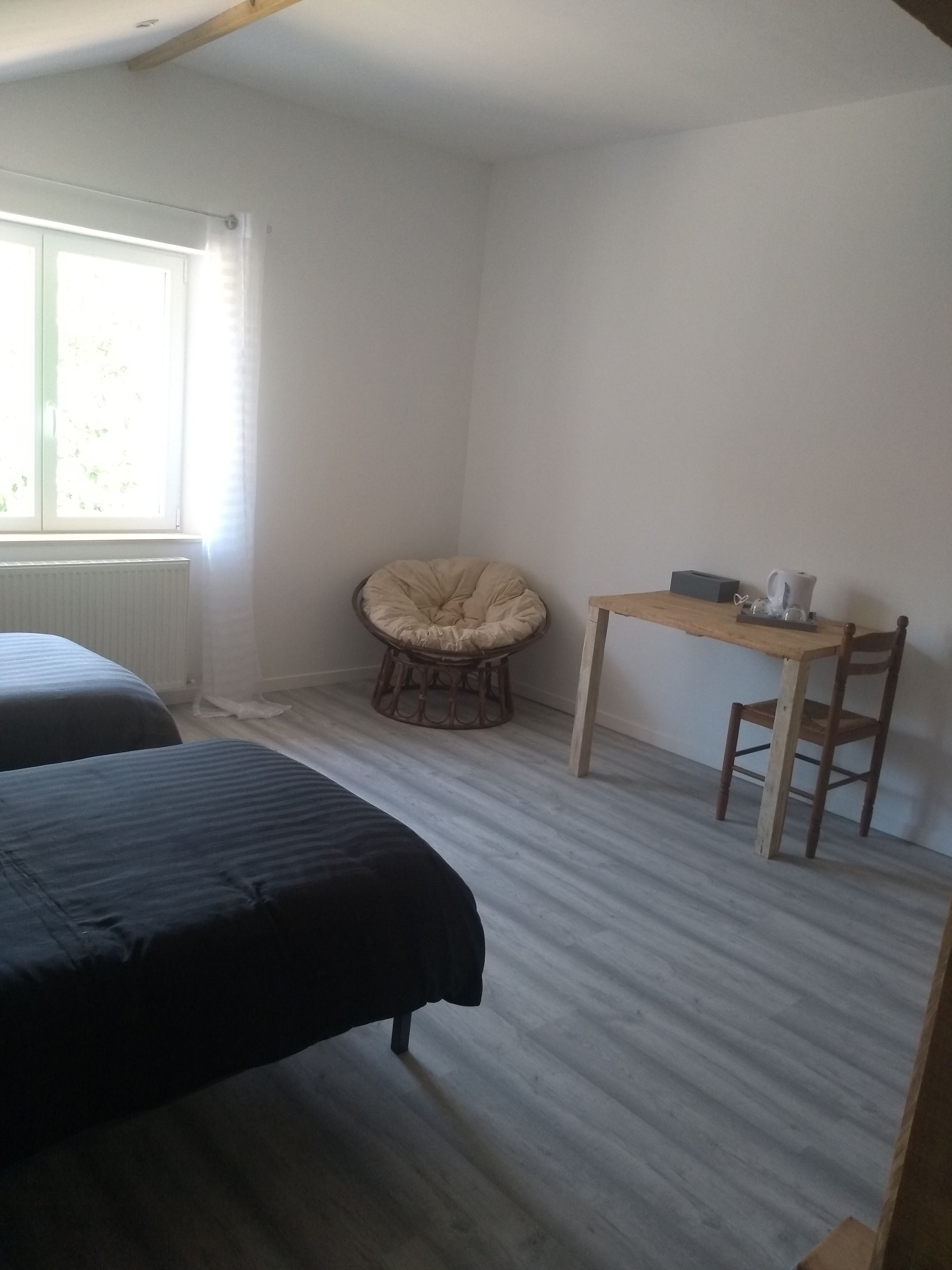 Una habitación con dos camas, una silla, una mesita y un ventanal.