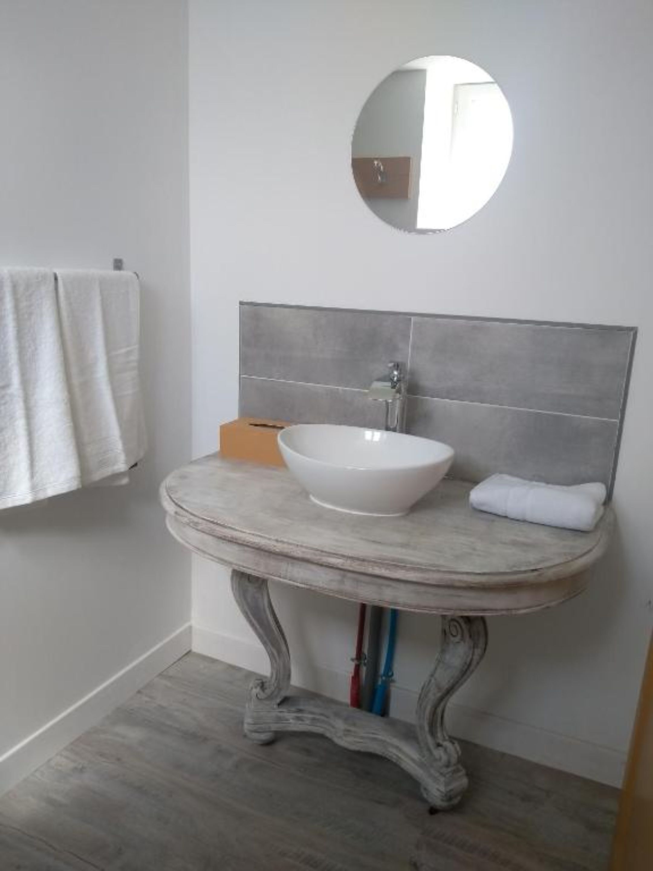 Ein Badezimmer mit einem weißen Waschbecken, einem runden Spiegel und einem Handtuch an der Wand.