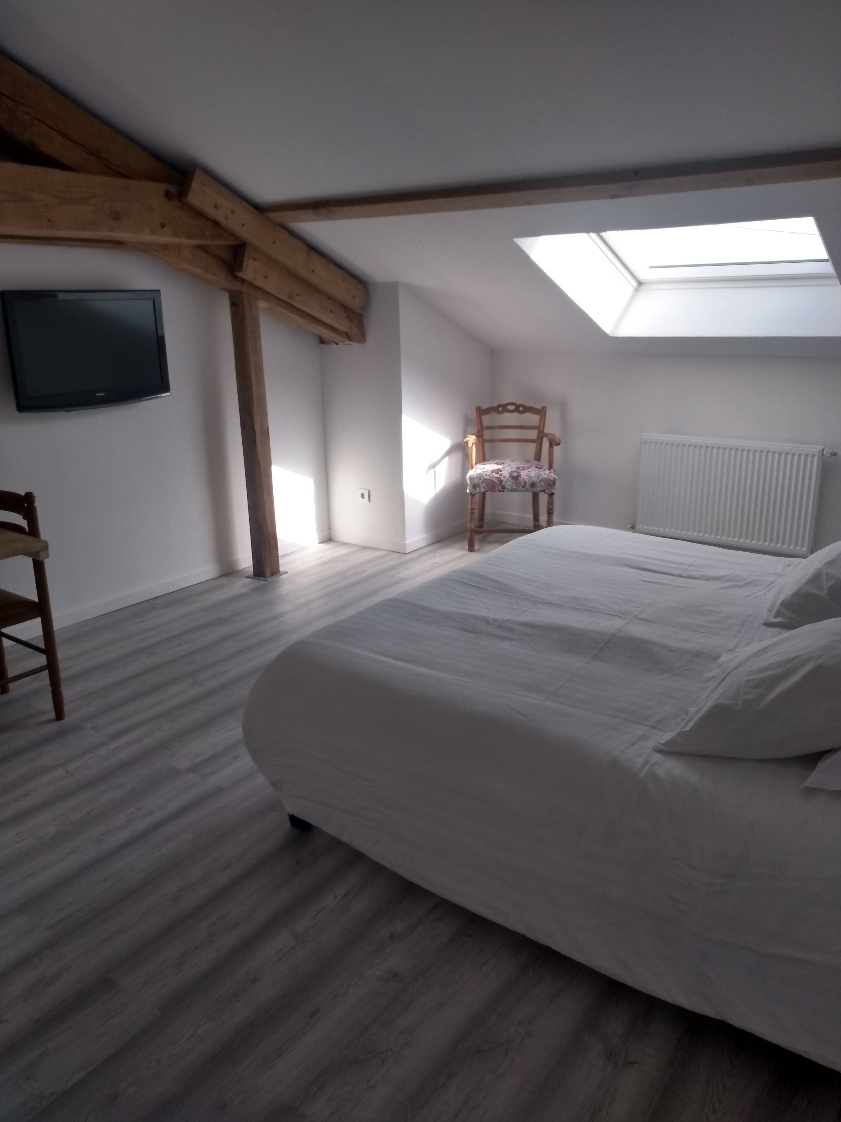 Un dormitorio con tragaluz, una cama, una silla y un televisor.
