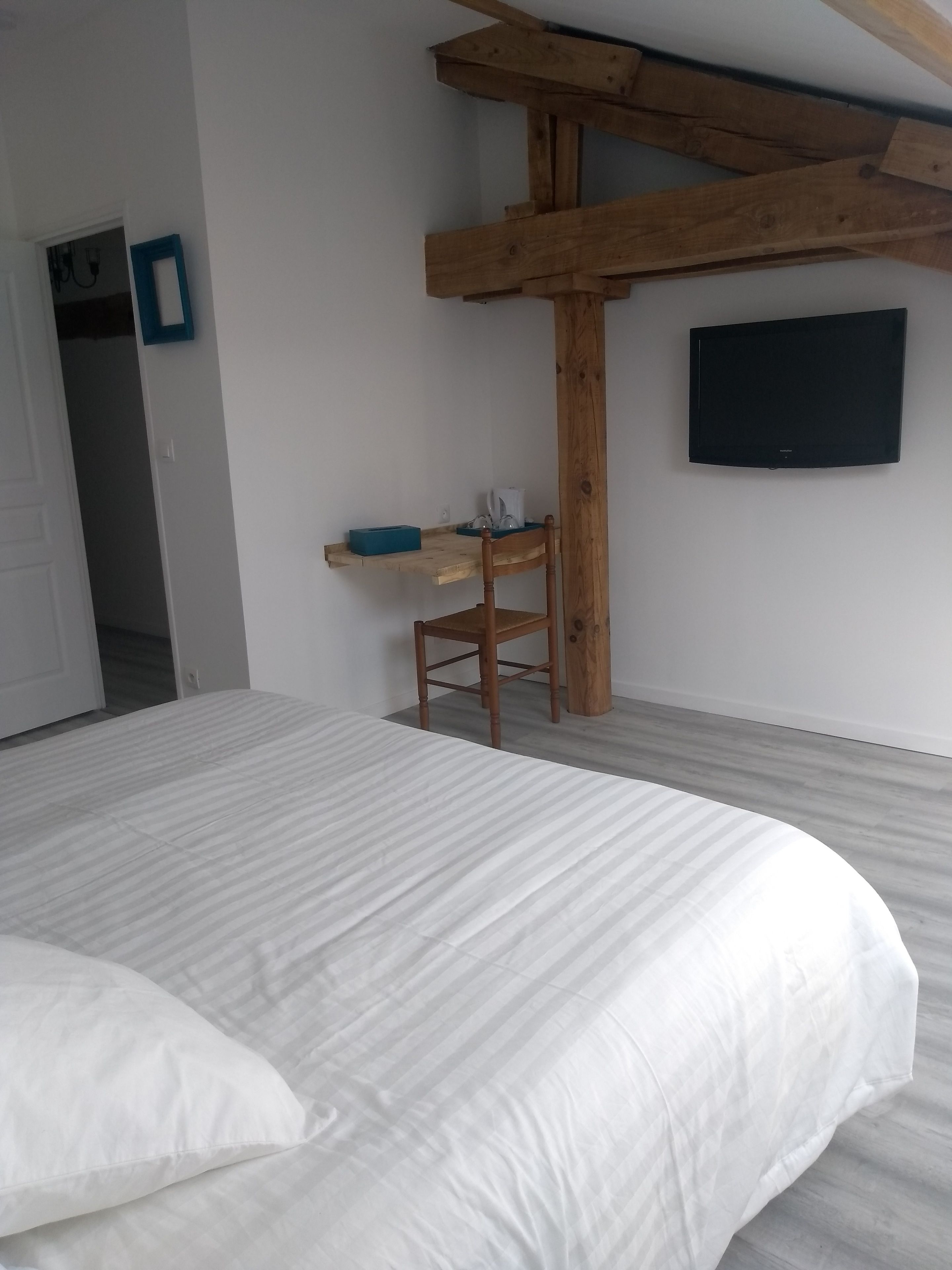 A bedroom with a bed, a wooden chair, a shelf, and a flat-screen TV mounted on the wall.