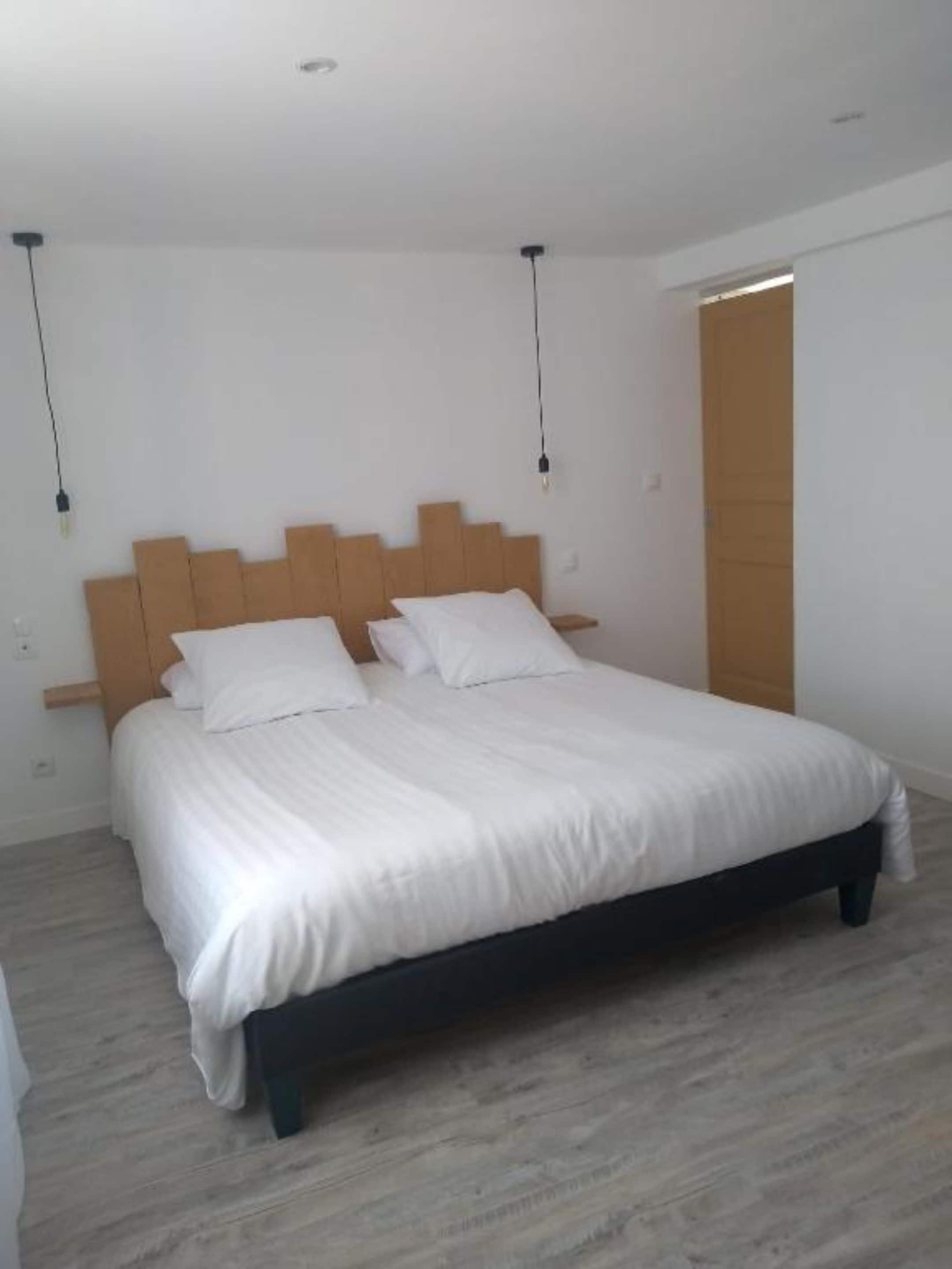 Une chambre à coucher avec une tête de lit en bois, un lit recouvert de linge de lit blanc et un plancher en bois.
