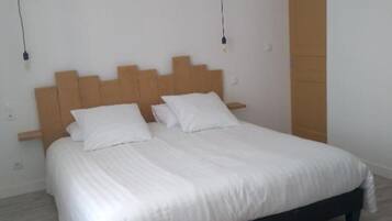 Une chambre à coucher avec une tête de lit en bois, un lit recouvert de linge de lit blanc et un plancher en bois.