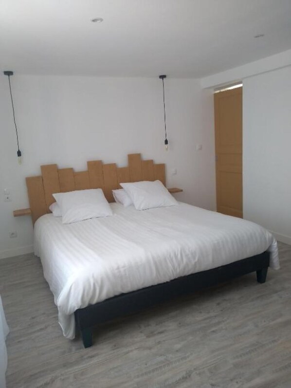 A bedroom with a wooden headboard, a bed with white bedding, and a wooden floor. - La maison de pescate (Souprousse)