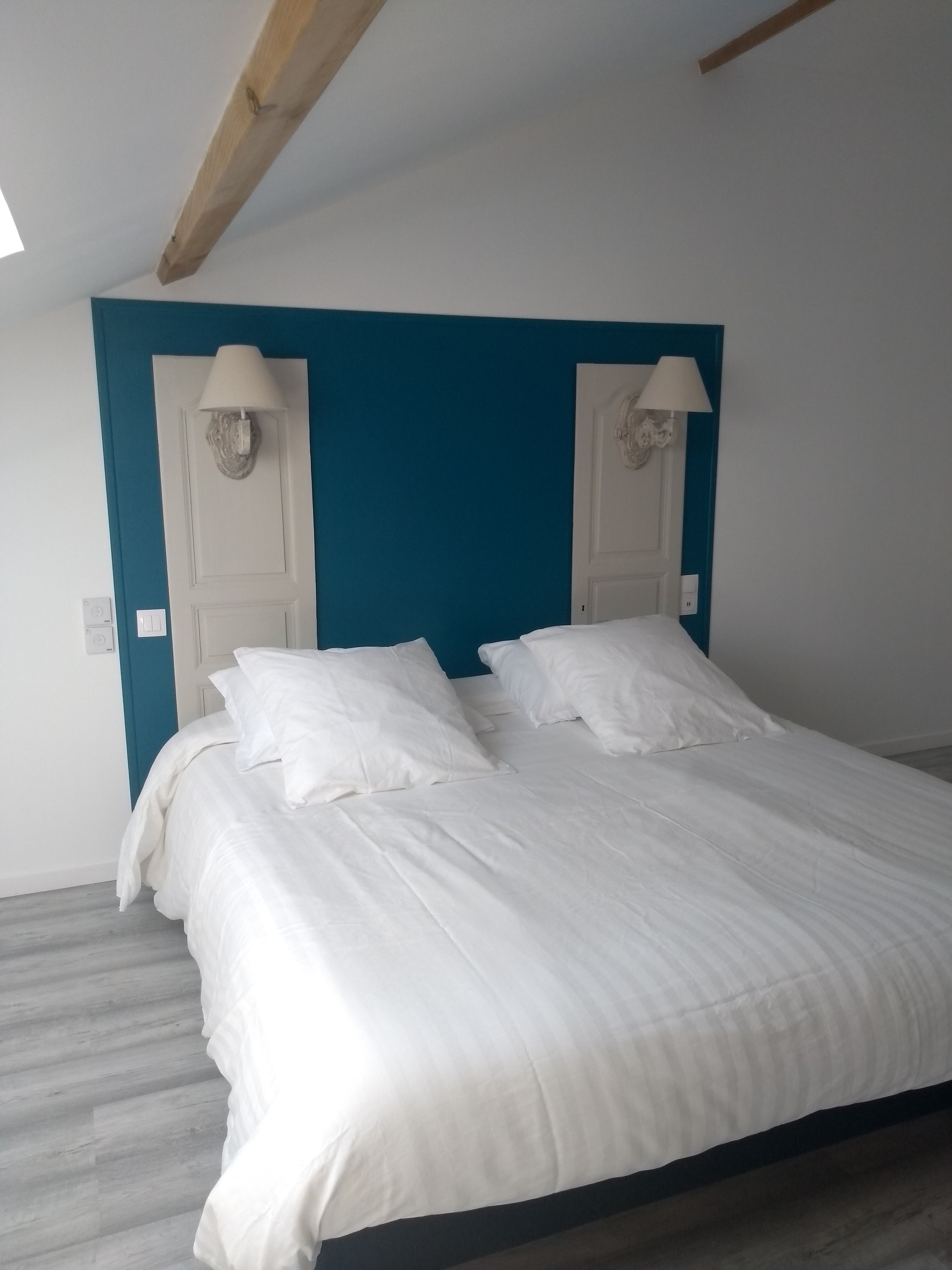 Un dormitorio con una cama, ropa de cama blanca, dos lámparas fijadas a la pared y una pared de acento color aguamarina.