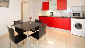 A modern kitchen with red cabinets, a white washing machine, and a dining area with a table and chairs. - La Marina by Interhome (Benissa)