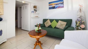 A living room with a green sofa, a round wooden table, and a painting of a sunset. - La Marina by Interhome (Benissa)