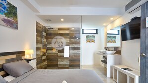 A modern hotel room with a large bed, a shower area, a sink, and a TV. - Colonial Beach House (Santo Domingo)