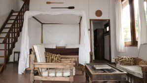 Une pièce avec un lit sous un dais, un escalier en bois, un canapé et une table basse.