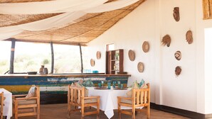 Un espace repas avec des chaises et des tables en bois, un toit de chaume et des œuvres d’art décoratives sur les murs.