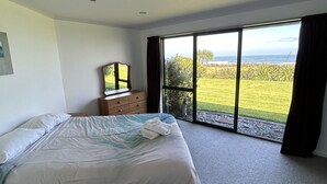 Een slaapkamer met een groot bed, een kast en uitzicht op een grasrijk landschap door een groot raam.