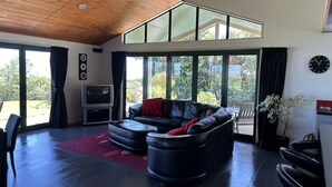 Een ruime woonkamer met een leren zwarte bank, een flatscreen televisie en een grote schuifdeur naar een tuin.