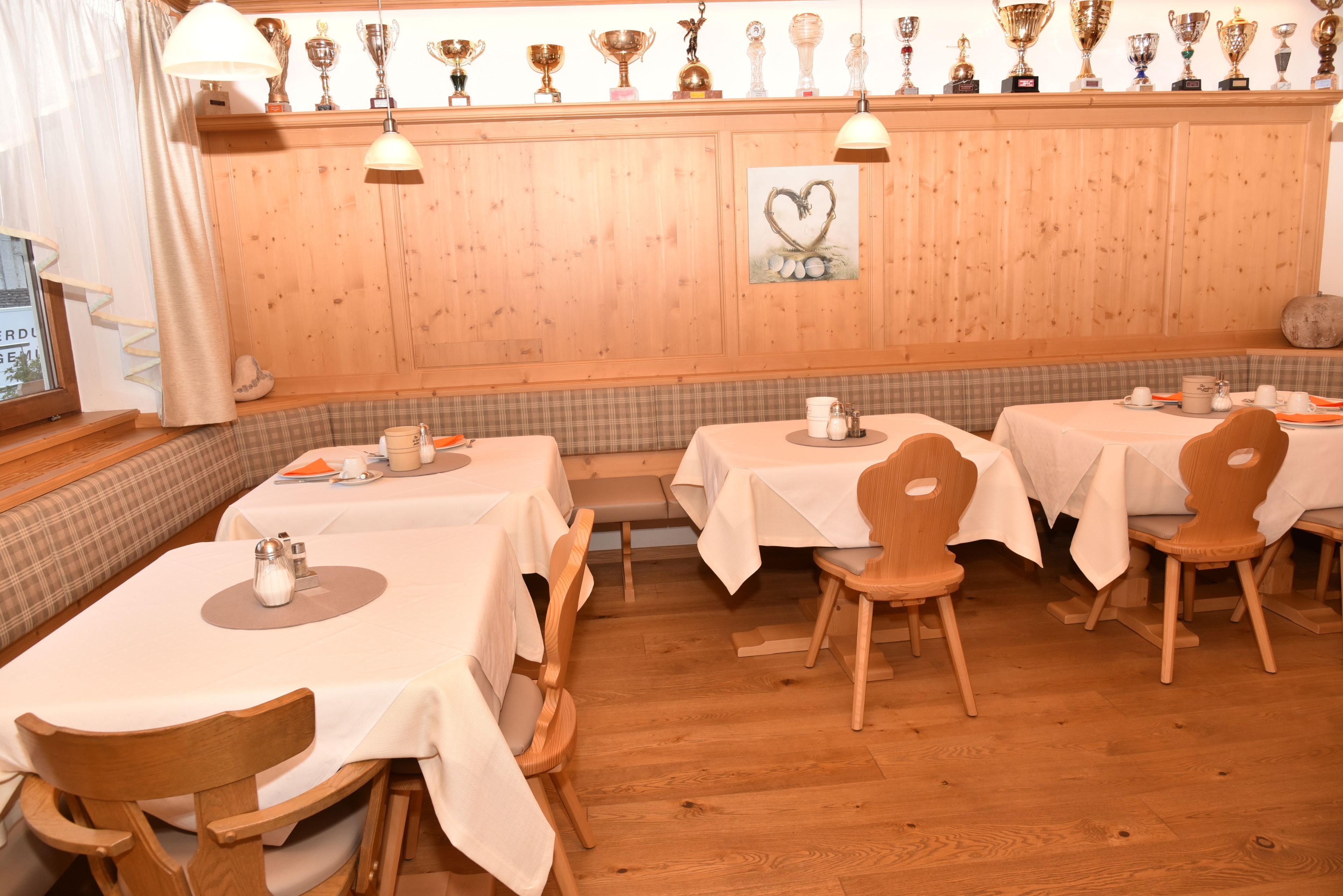 Ein Restaurant mit Holzwandverkleidung, mehreren Tischen mit weißen Tischdecken und Holzbänken.