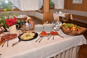 Una mesa de buffet con diversos alimentos, como frutas, verduras y carnes, dispuestas sobre un mantel blanco.