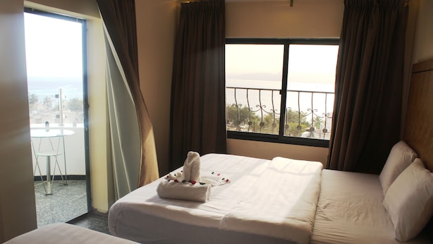 Habitación de hotel con dos camas, un balcón con vistas y una mesita con un control remoto.