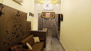 Un área de recepción con un sofá marrón, un panel decorativo en la pared, un Corán enmarcado y una pared de mármol.